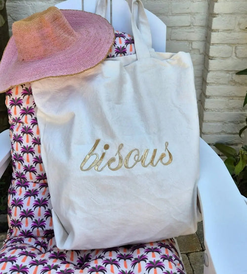 Gold embroidered bisous canvas tote bag and pink woven straw hat set for summer resortwear.