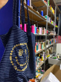Artisan gold floral embroidered navy pinstripe canvas tote bag displayed in a workshop setting.